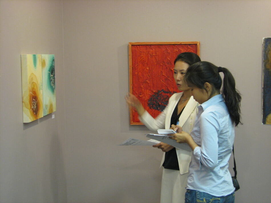 The artist speaking to a journalist in front of her paintings in a gallery