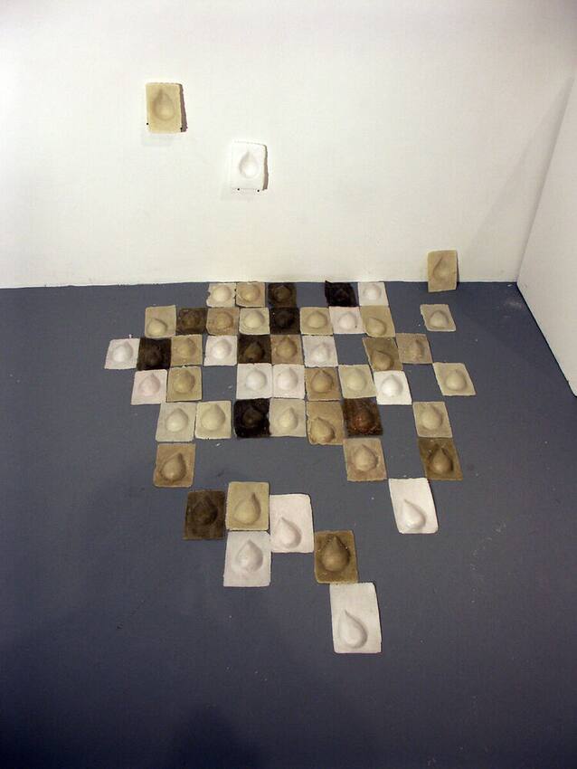 Installation — dozens of small plaster tiles, each holding a cast teardrop, arranged across the floor and rising onto the wall
