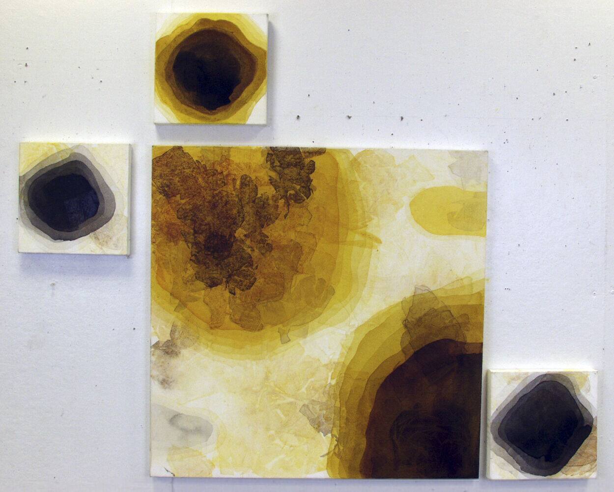 Installation — a large panel of layered amber and ochre pressed leaves on a white wall, surrounded by three small square panels each holding a concentric ring of colour